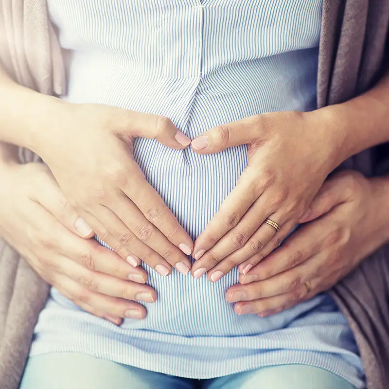 Pregnant woman with man both holding their hands in hearts on her belly - Bible verses about abortion