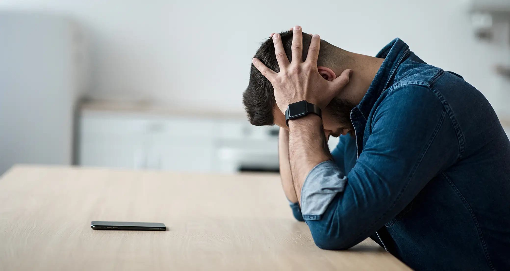 Man sitting at a table with his hands on his head. Bible verses about stress